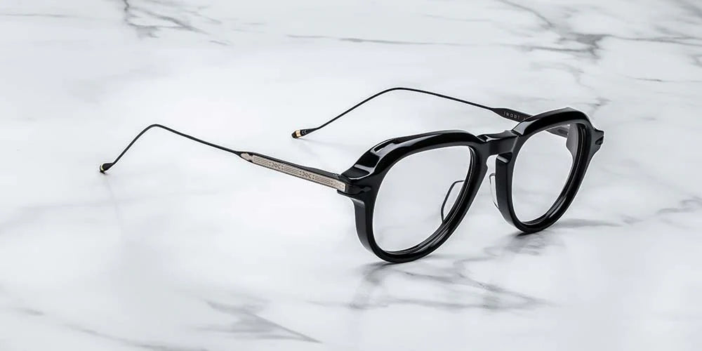 A pair of black '50s-inspired aviator optical glasses with wirecore temples and a unique front-pin hinge design, laying on a marble surface. side view