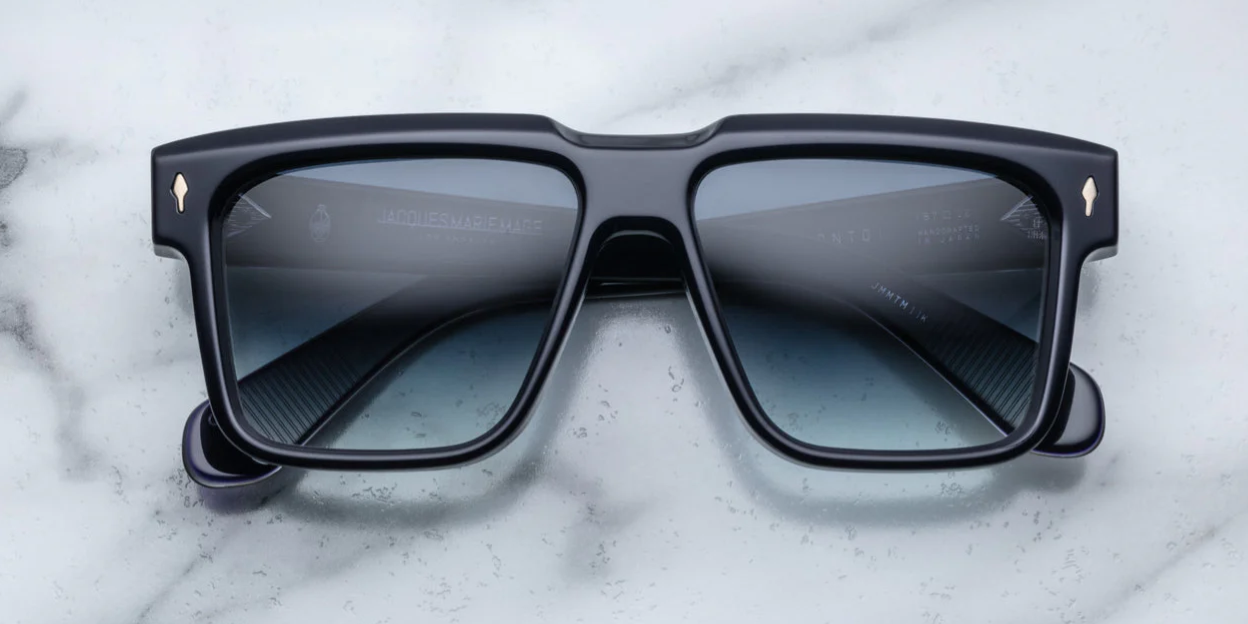 A pair of black rectangular framed sunglasses with a sculptural brow, resting on a marble surface.