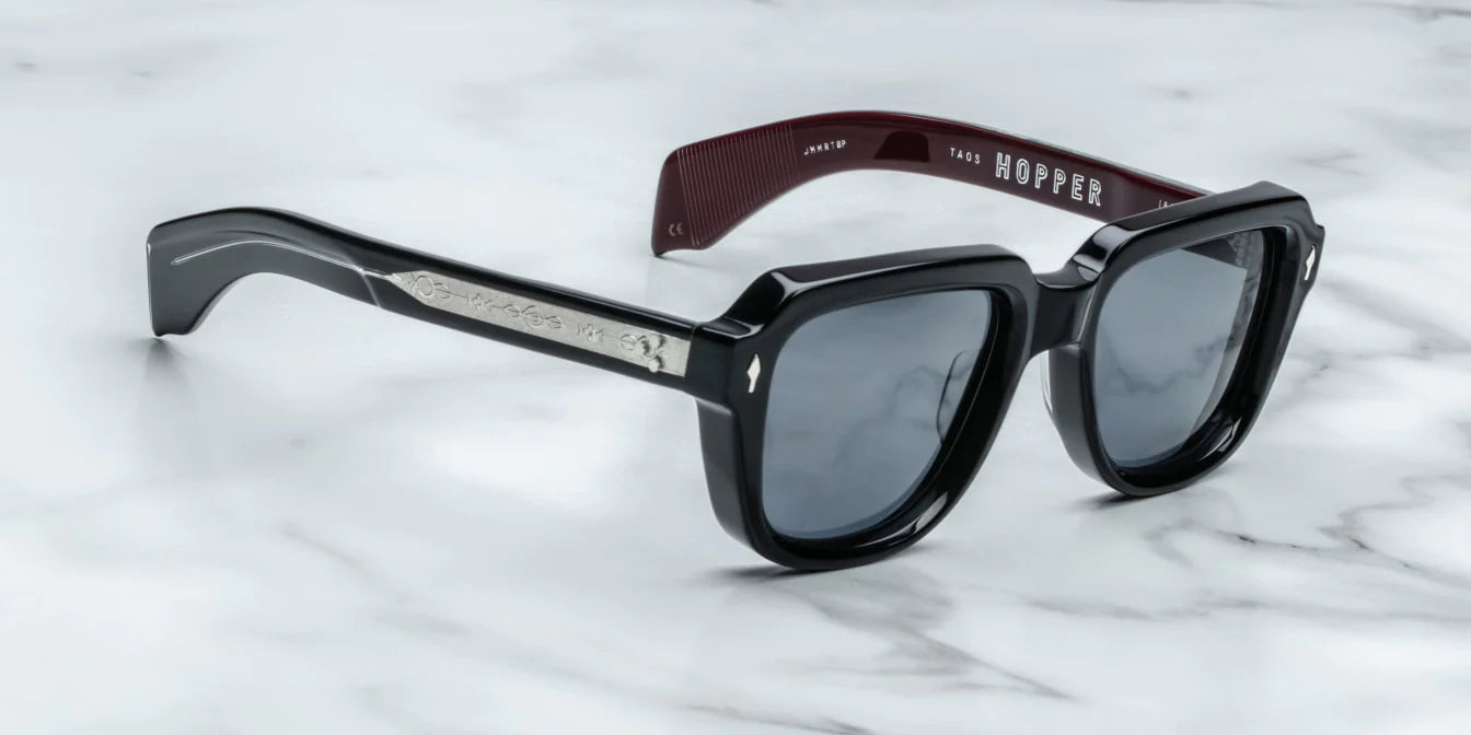 A pair of black sunglasses with distinctive 60s-inspired design, featuring bloodstone accents on the arms.