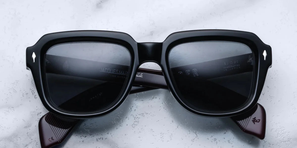 A pair of black sunglasses with distinctive 60s-inspired design, featuring bloodstone accents on the arms.