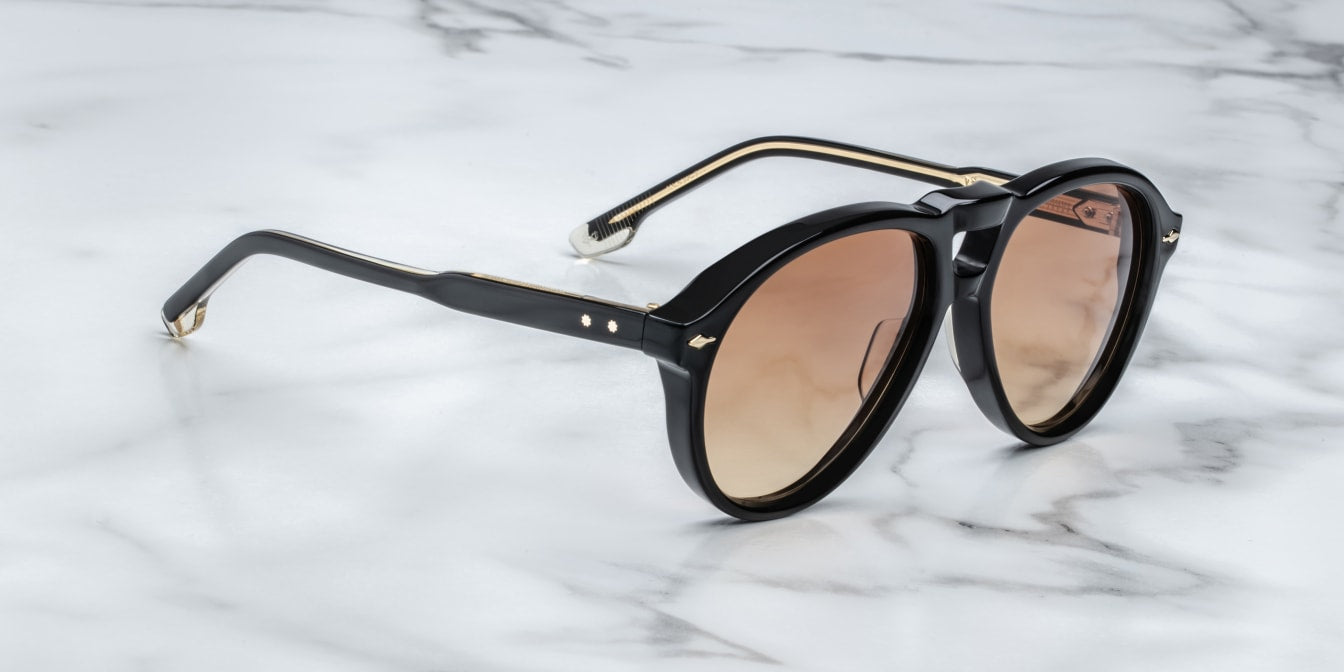 A pair of '80s-inspired oversized aviator sunglasses with a black frame and bronze-colored lenses, placed on a marble surface. side view