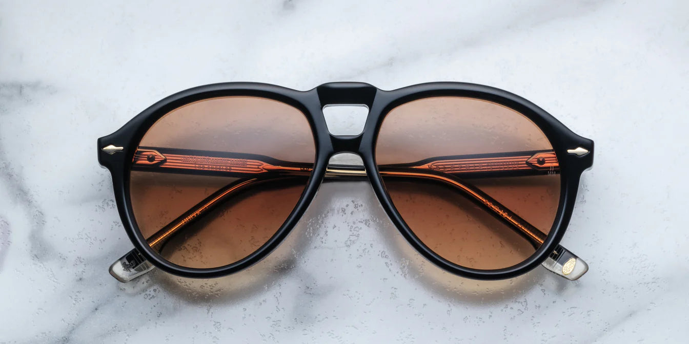 A pair of '80s-inspired oversized aviator sunglasses with a black frame and bronze-colored lenses, placed on a marble surface.
