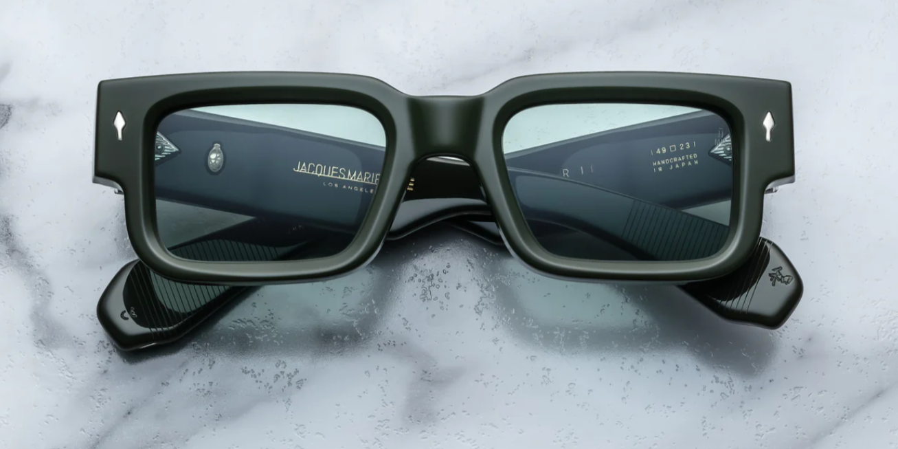 A pair of rectangular, dark green sunglasses with custom double-laminated temples and wirecores, on a marble surface.