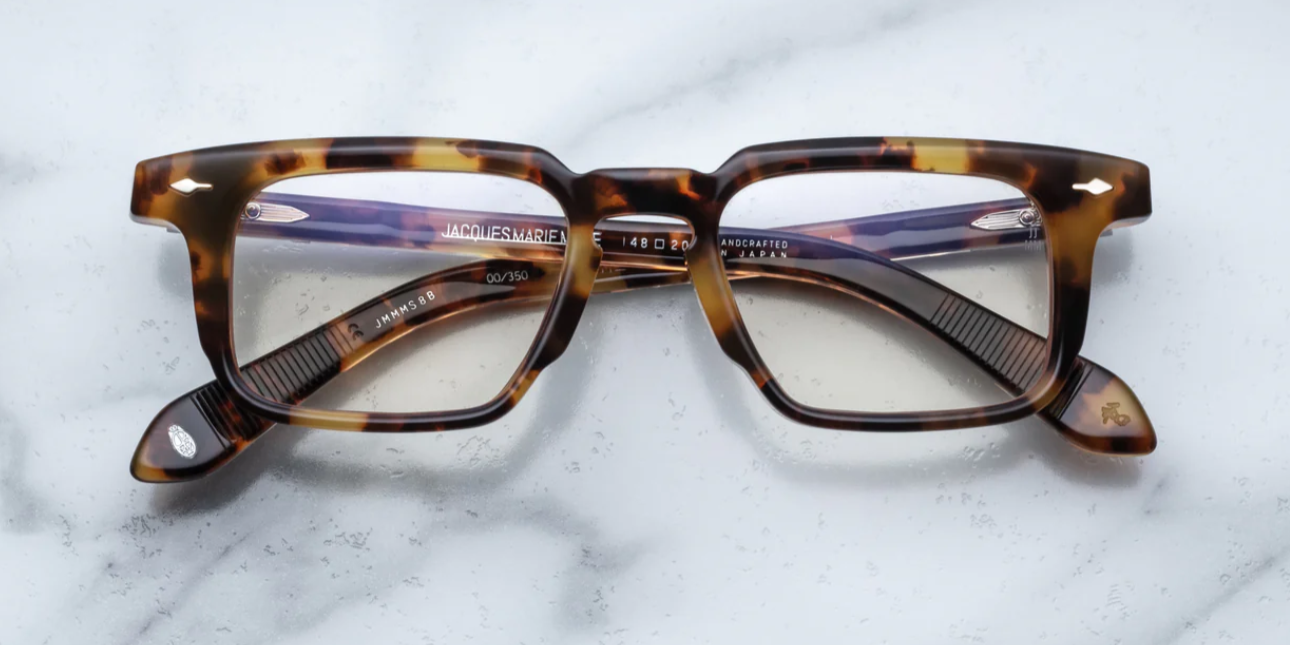 A pair of Jacques Marie Mage eyeglasses with a strong rectangular lens shape, titanium hinges, and wirecore temples with engraved details, in a Havana style pattern.