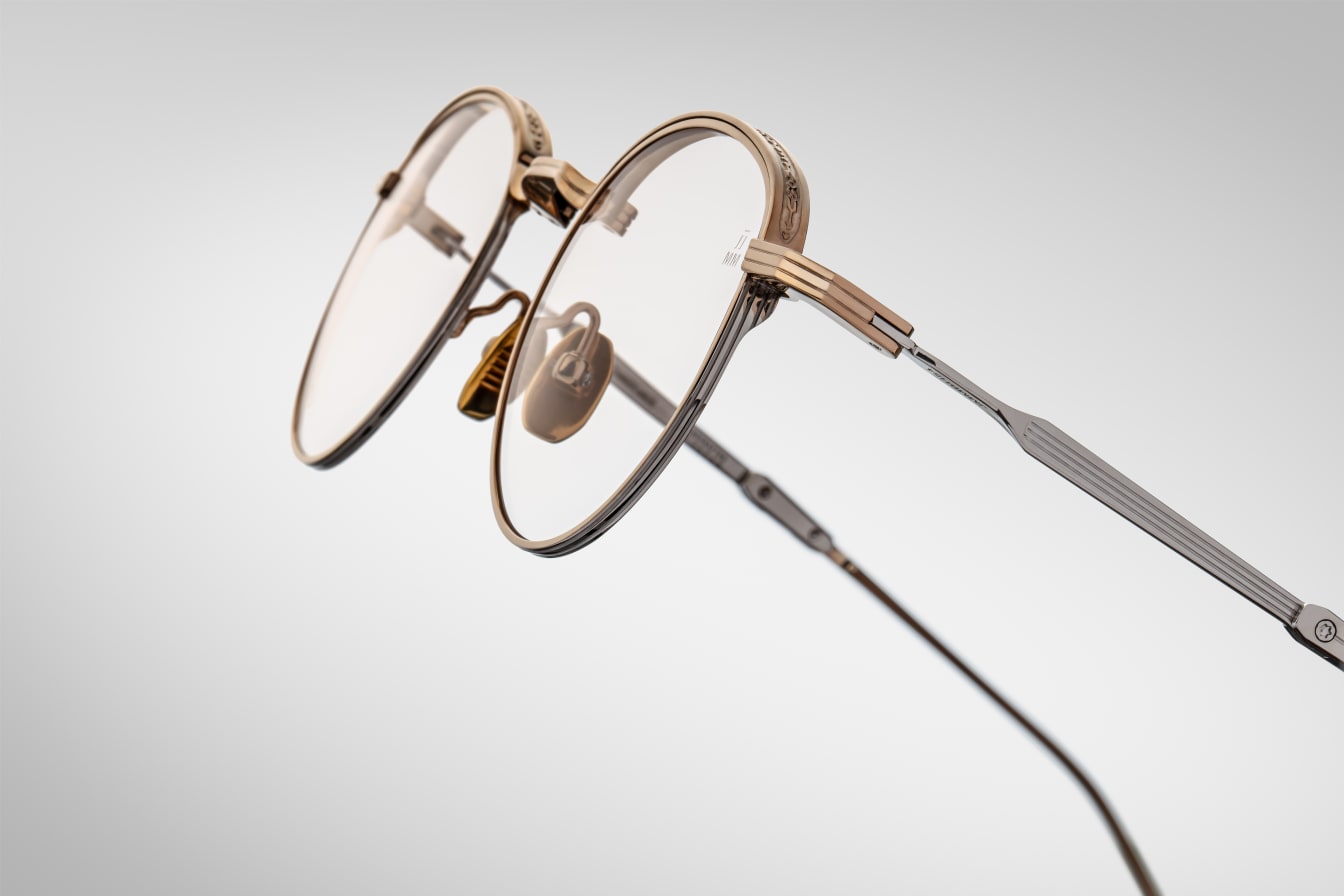 Pair of round eyeglasses with gold frame on a light gray background