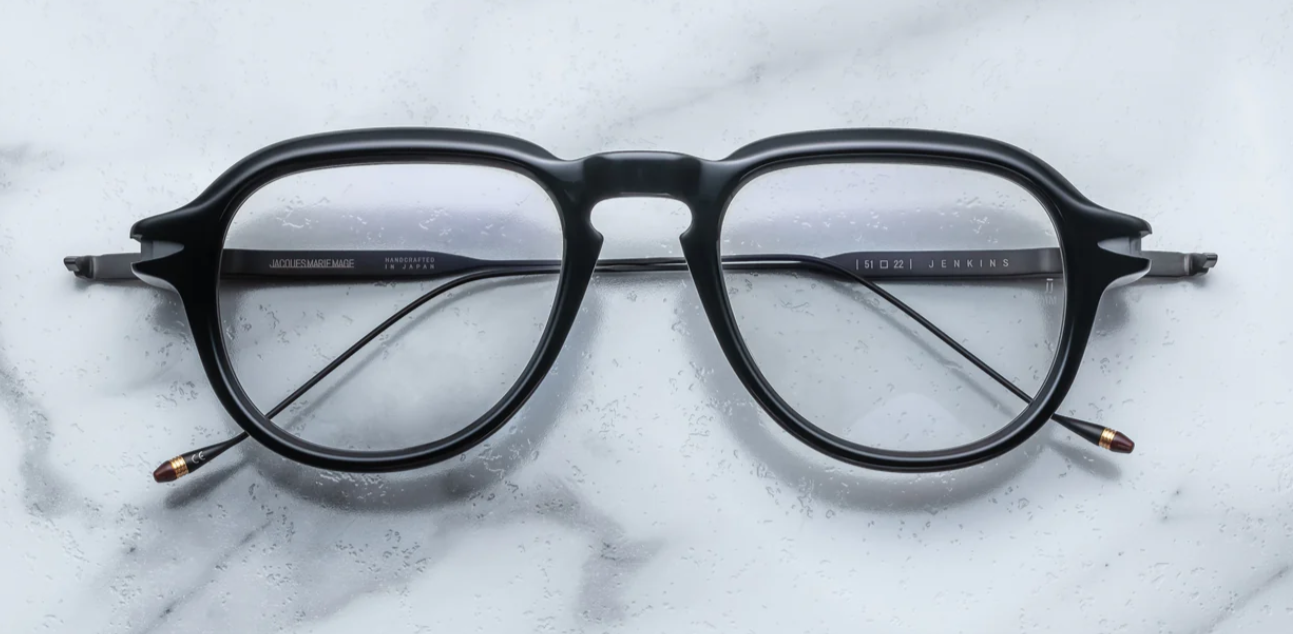 A pair of black '50s-inspired aviator optical glasses with wirecore temples and a unique front-pin hinge design, laying on a marble surface.