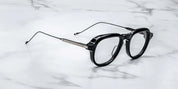 A pair of black '50s-inspired aviator optical glasses with wirecore temples and a unique front-pin hinge design, laying on a marble surface. side view