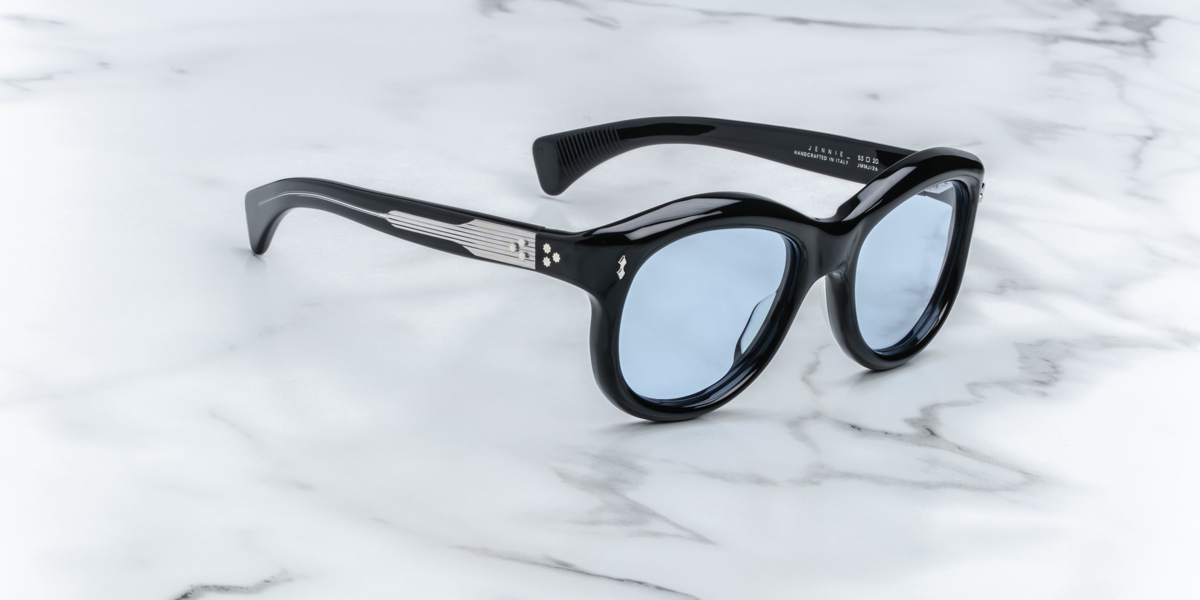 A pair of sunglasses in black, placed on a marble surface. side view