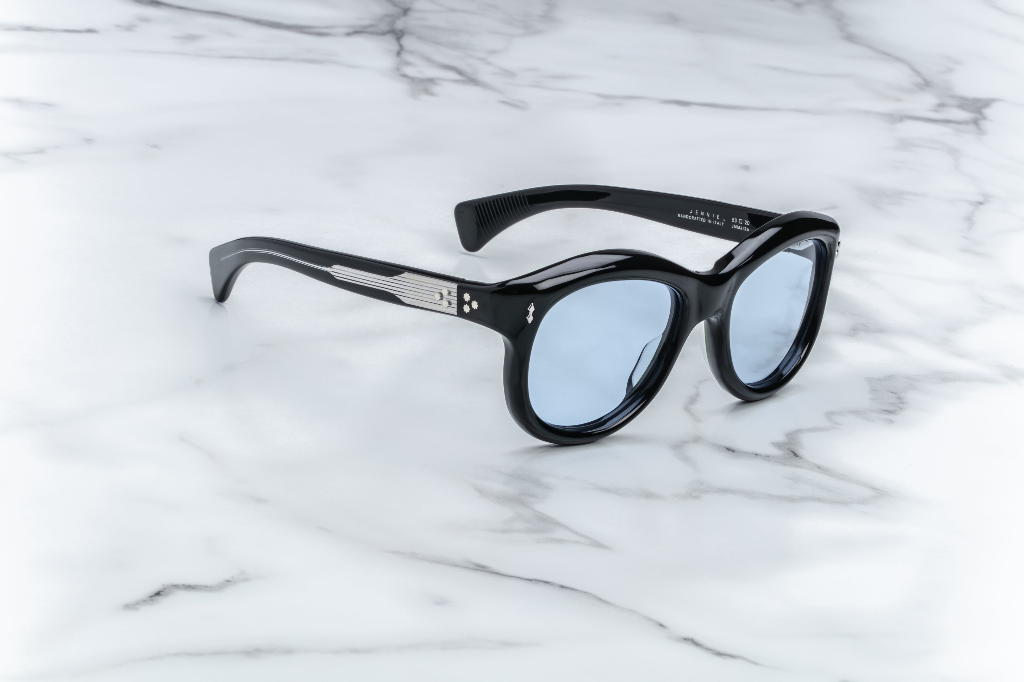 A pair of sunglasses in black, placed on a marble surface. side view