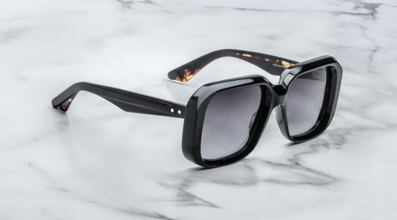 A pair of black, rectangular '70s-inspired sunglasses with sculptural temples and polished metal details, displayed on a marble surface. side view