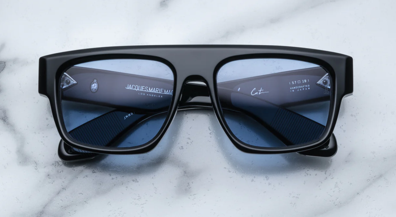 A pair of black sunglasses with distinctive browline and sculptural temples, featuring signature precious metal embellishments.