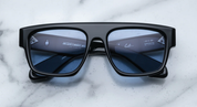 A pair of black sunglasses with distinctive browline and sculptural temples, featuring signature precious metal embellishments.