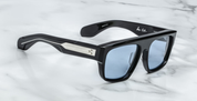 A pair of black sunglasses with distinctive browline and sculptural temples, featuring signature precious metal embellishments.