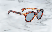 A pair of sunglasses with a leopard print frame, placed on a marble surface side view