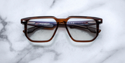 A pair of Jacques Marie Mage Saburo optical frames with a hickory color and navigator-style design, featuring handcrafted acetate and signature floating hinges.