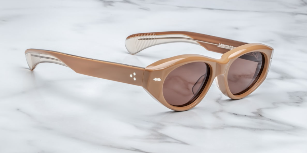 A pair of cat-eye style sunglasses with tobacco brown frame and lenses, featuring a double-arrowhead front pin and rounded paddle temples on a marble surface. side view