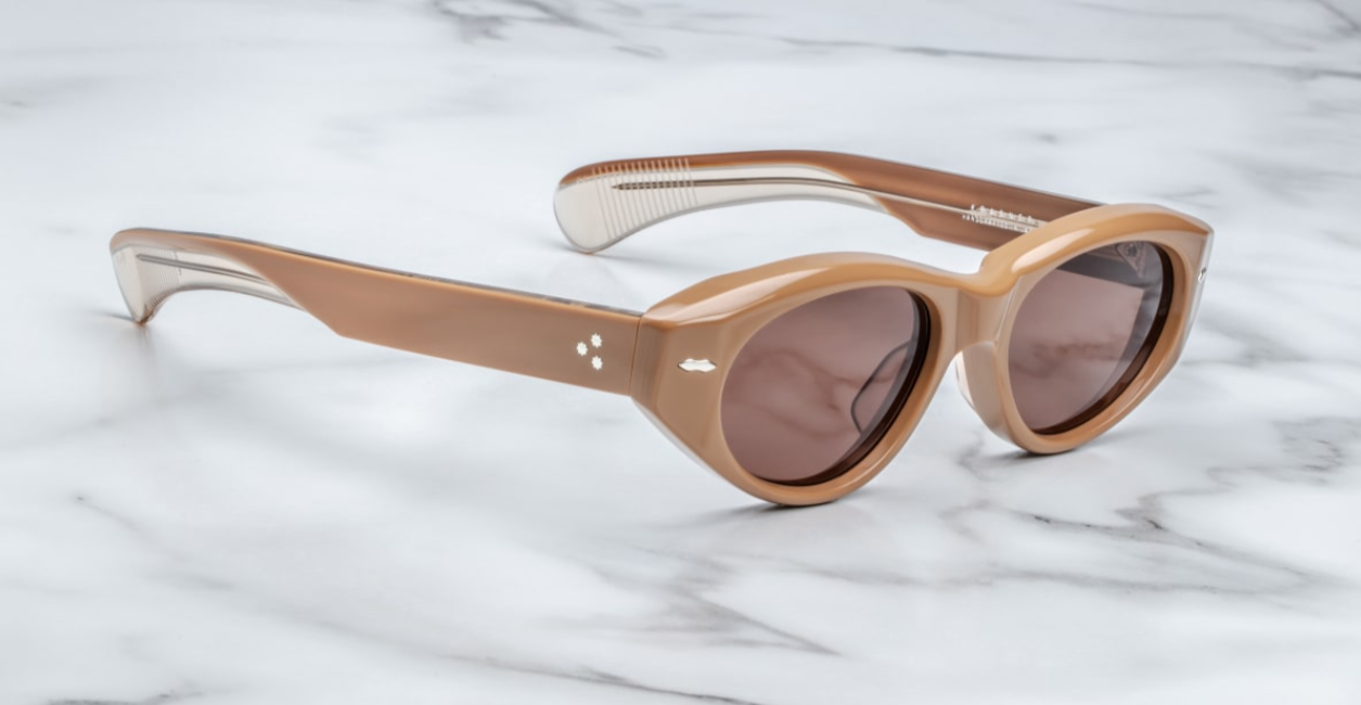 A pair of cat-eye style sunglasses with tobacco brown frame and lenses, featuring a double-arrowhead front pin and rounded paddle temples on a marble surface. side view