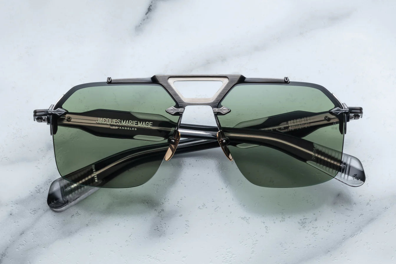 A pair of rimless sunglasses with a gunmetal frame, titanium nose-and-brow bridge, dual-tone details, sculptural acetate temples, and wirecore embellishments.