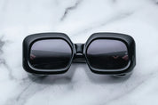 A pair of black, rectangular, '70s-inspired sunglasses with a marble background.