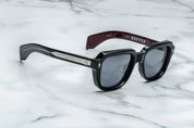 A pair of black sunglasses with distinctive 60s-inspired design, featuring bloodstone accents on the arms.