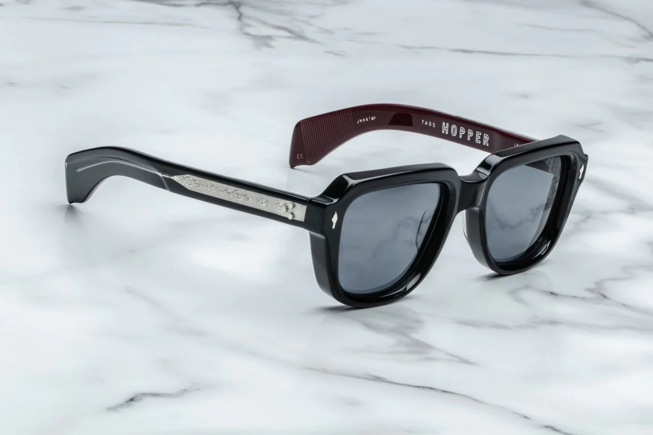 A pair of black sunglasses with distinctive 60s-inspired design, featuring bloodstone accents on the arms.