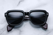A pair of black sunglasses with distinctive 60s-inspired design, featuring bloodstone accents on the arms.