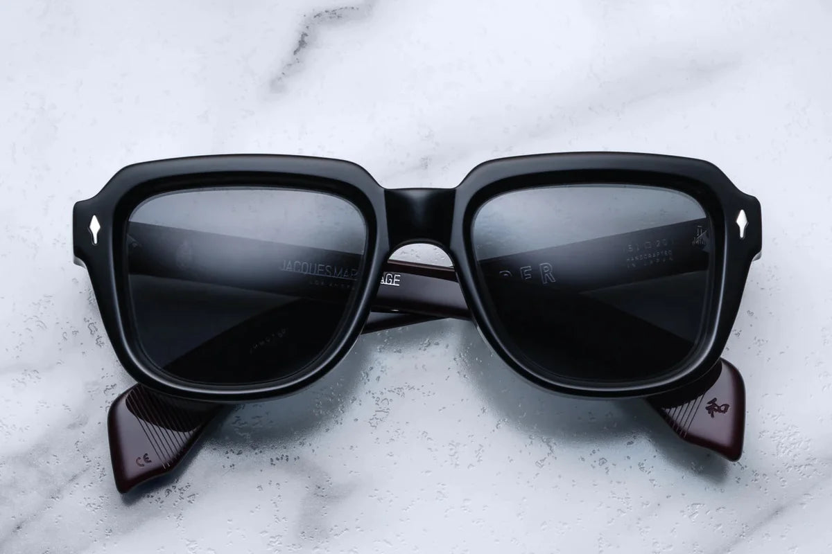 A pair of black sunglasses with distinctive 60s-inspired design, featuring bloodstone accents on the arms.