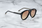 A pair of '80s-inspired oversized aviator sunglasses with a black frame and bronze-colored lenses, placed on a marble surface. side view