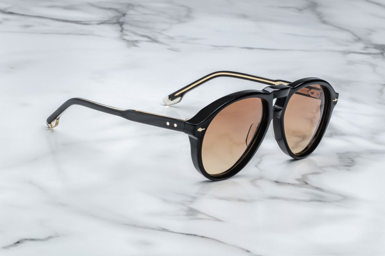 A pair of '80s-inspired oversized aviator sunglasses with a black frame and bronze-colored lenses, placed on a marble surface. side view
