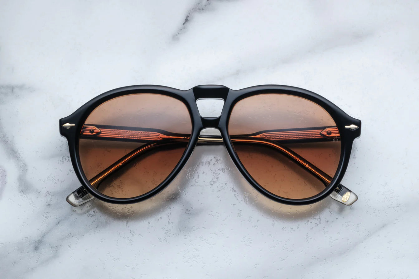 A pair of '80s-inspired oversized aviator sunglasses with a black frame and bronze-colored lenses, placed on a marble surface.