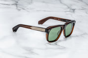 Sunglasses with brown frame and green lenses on a marble surface side view with gold metal detail on temples