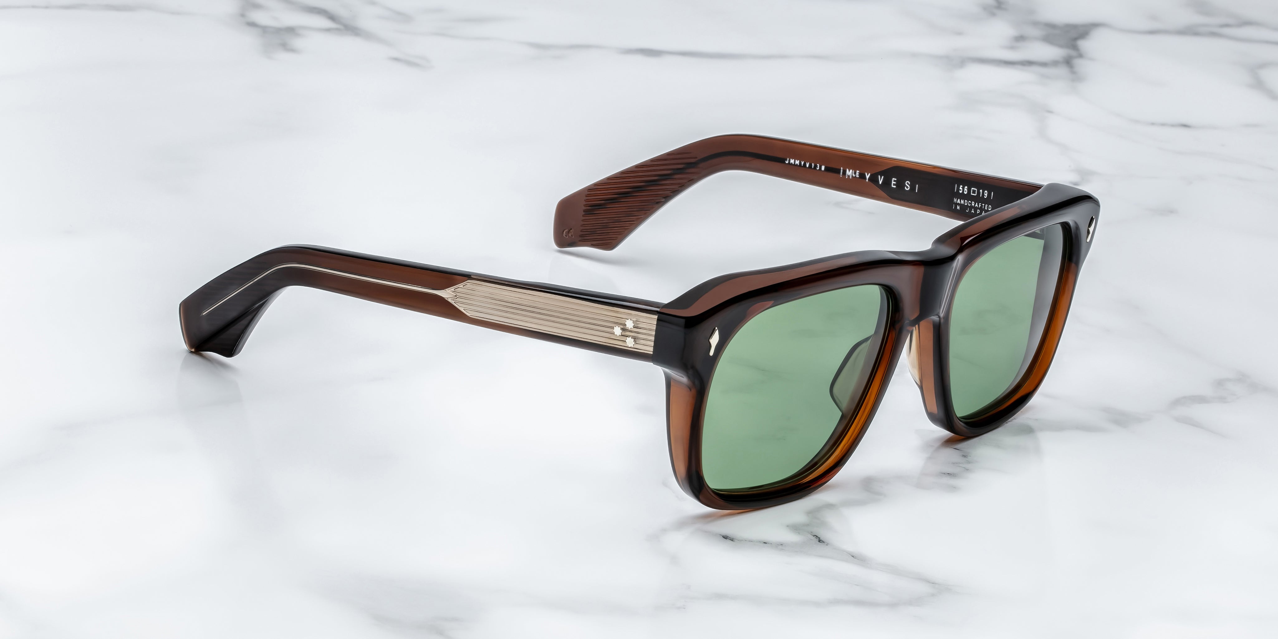 Sunglasses with brown frame and green lenses on a marble surface side view with gold metal detail on temples