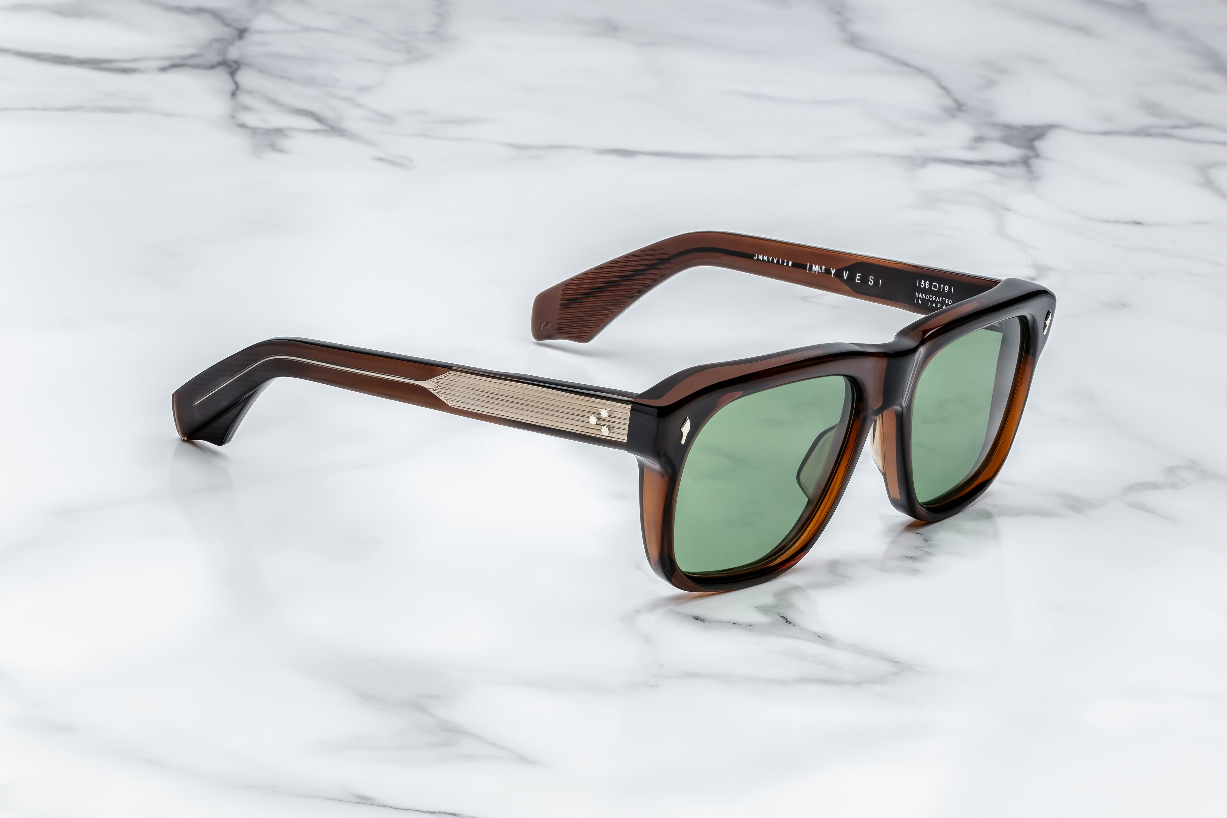 Sunglasses with brown frame and green lenses on a marble surface side view with gold metal detail on temples