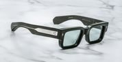 A pair of rectangular, dark green sunglasses with custom double-laminated temples and wirecores, on a marble surface. side view