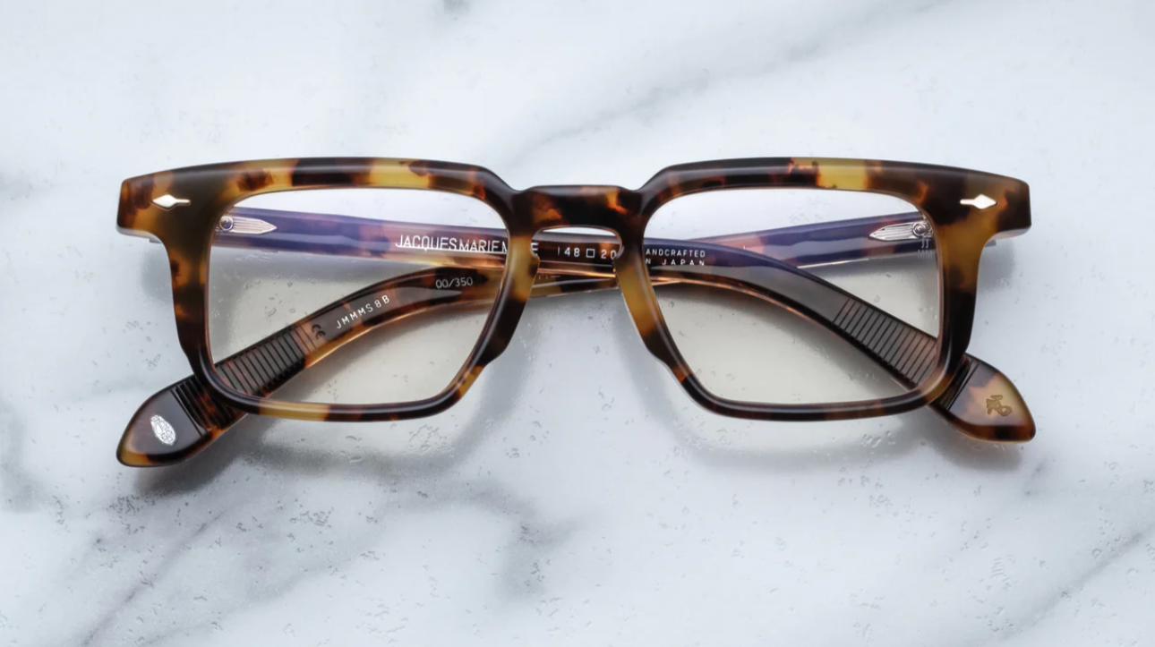 A pair of Jacques Marie Mage eyeglasses with a strong rectangular lens shape, titanium hinges, and wirecore temples with engraved details, in a Havana style pattern.