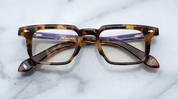 A pair of Jacques Marie Mage eyeglasses with a strong rectangular lens shape, titanium hinges, and wirecore temples with engraved details, in a Havana style pattern.